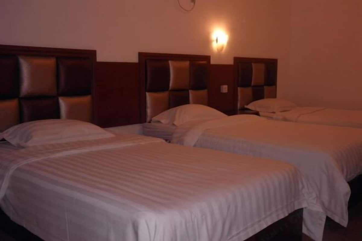 Una habitación de hotel con tres camas individuales, cabeceros de madera y una lámpara de pared.