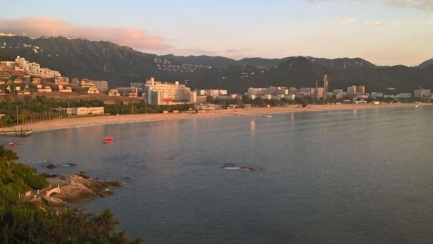 Een kuststadsbeeld met gebouwen, een strand en bergen op de achtergrond.