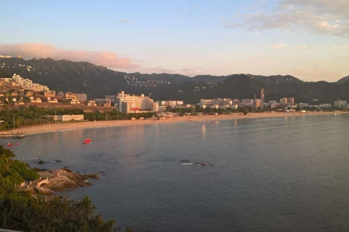 Un paisaje urbano costero con edificios, una playa y montañas al fondo.