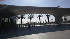 Een overdekt buitengebied met palmbomen en een moderne architectuur.