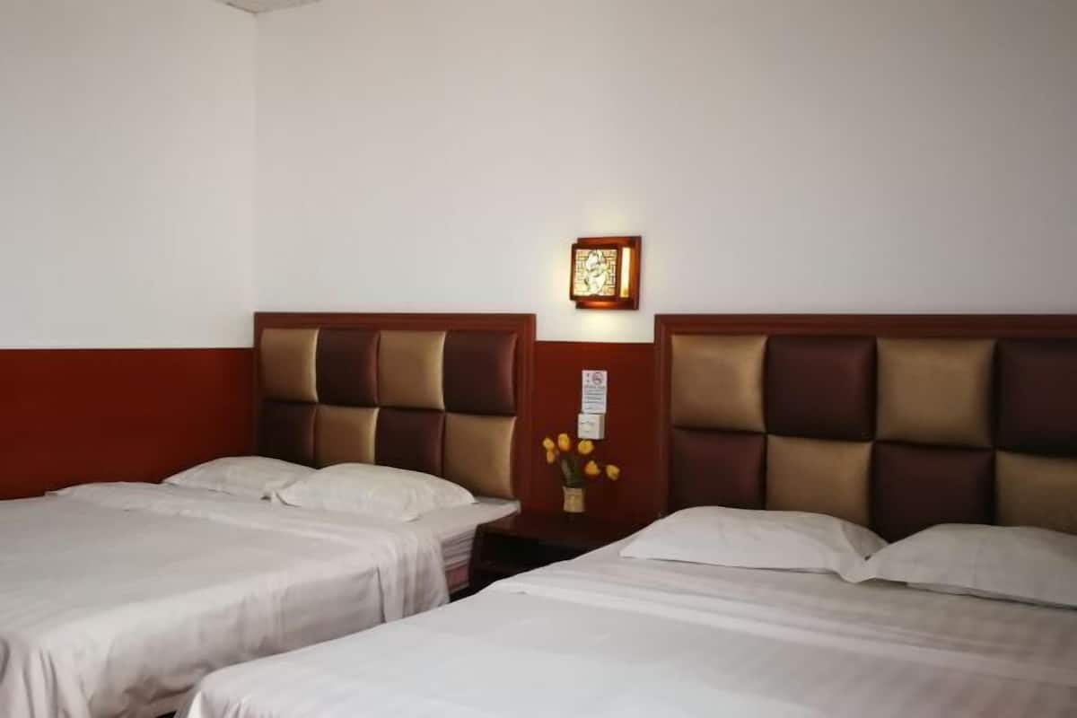 Habitación de hotel con dos camas, cabecera de madera, una mesita con un florero y un cuadro en la pared.