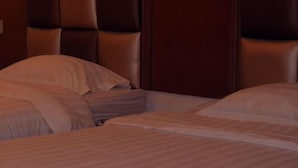 Een hotelkamer met een groot bed, een hoofdeinde met een gestoffeerd ontwerp, en een houten hoofdeinde aan de rechterkant.