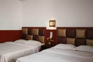 Une chambre d’hôtel avec deux lits, une table de chevet, une lampe fixée au mur et un vase avec des fleurs.