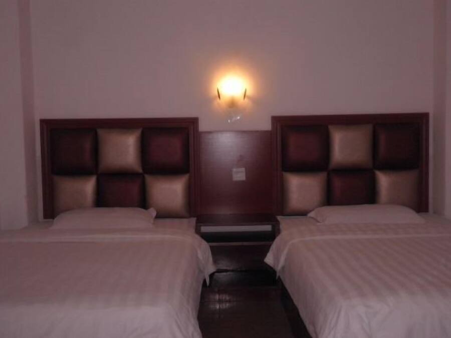 Habitación de hotel con dos camas, una mesita de noche central y una lámpara fijada a la pared.