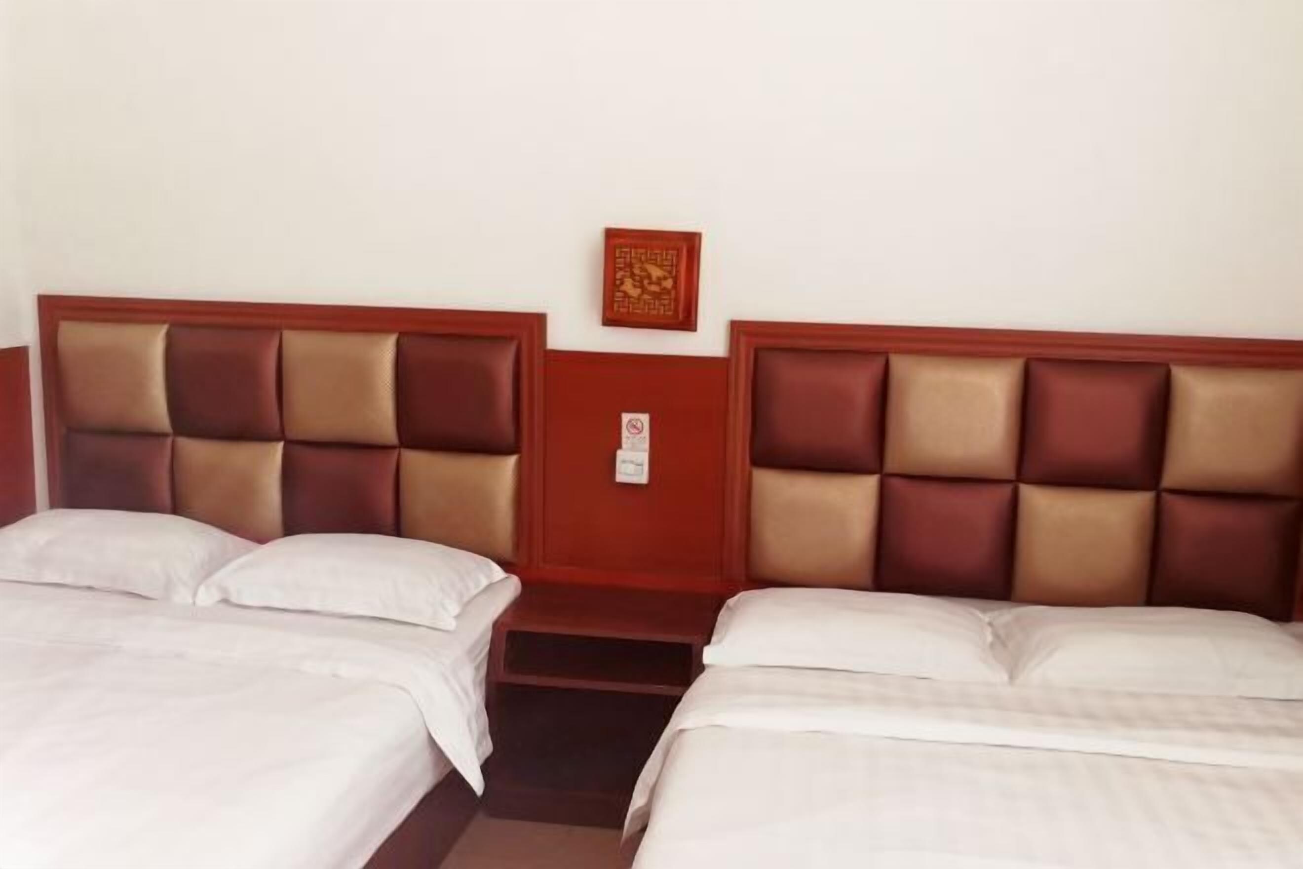Quarto de hotel com duas camas, cabeceira de madeira, uma mesinha e um objeto decorativo na parede.
