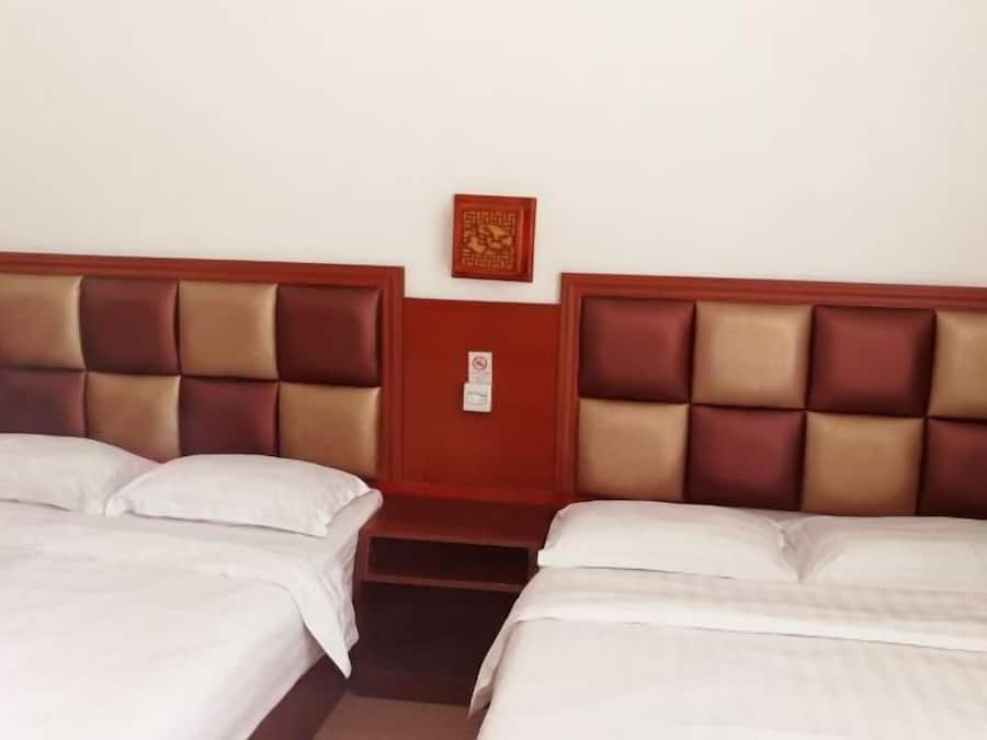 Quarto de hotel com duas camas, cabeceira de madeira, uma mesinha e um objeto decorativo na parede.