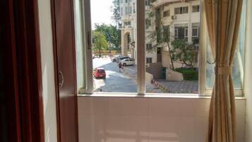 A view from a window with curtains, overlooking a street with parked cars and buildings in the background.