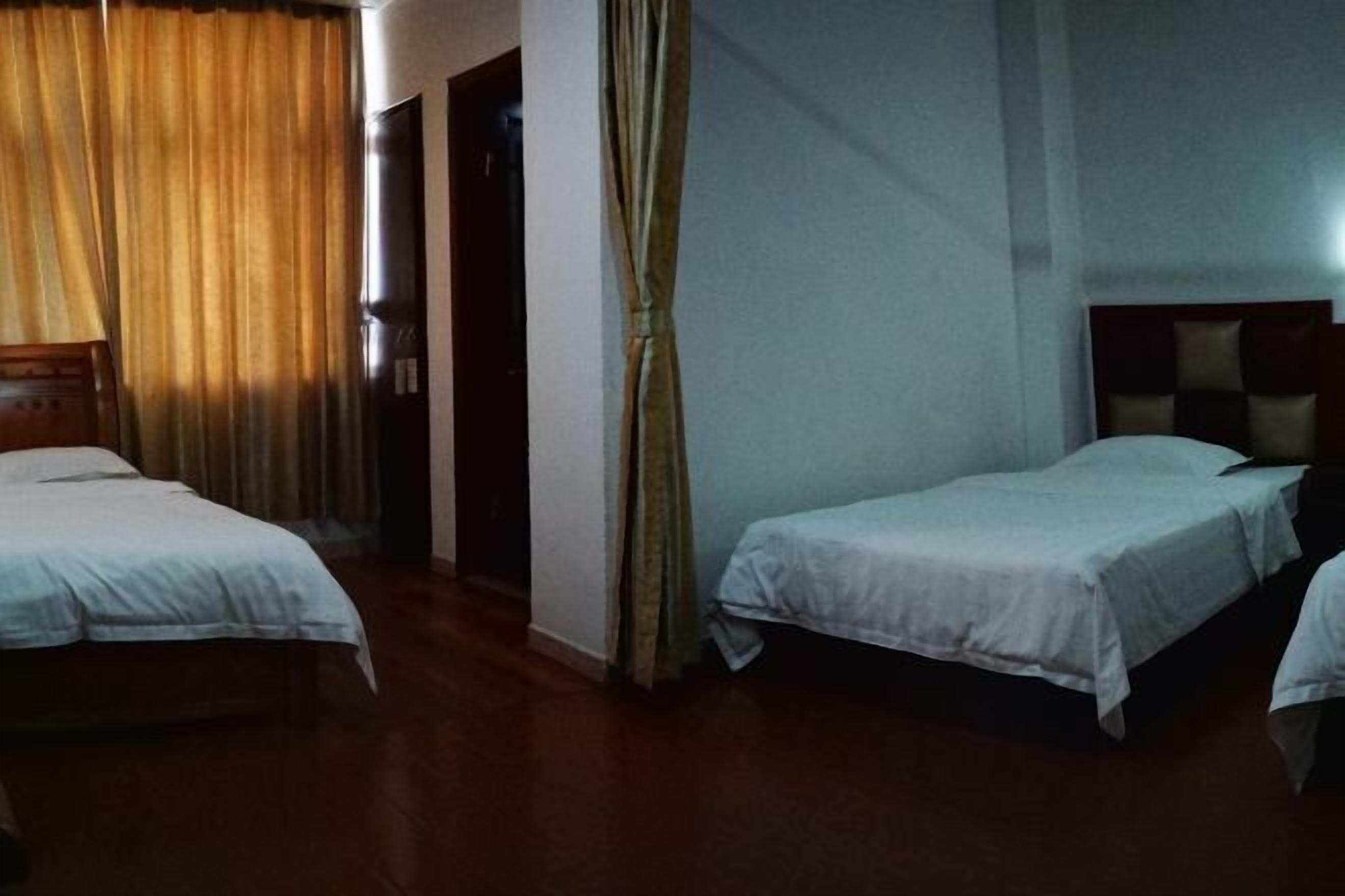 Quarto de hotel com duas camas, uma cortina, uma porta e um aparelho de luz fixado na parede.