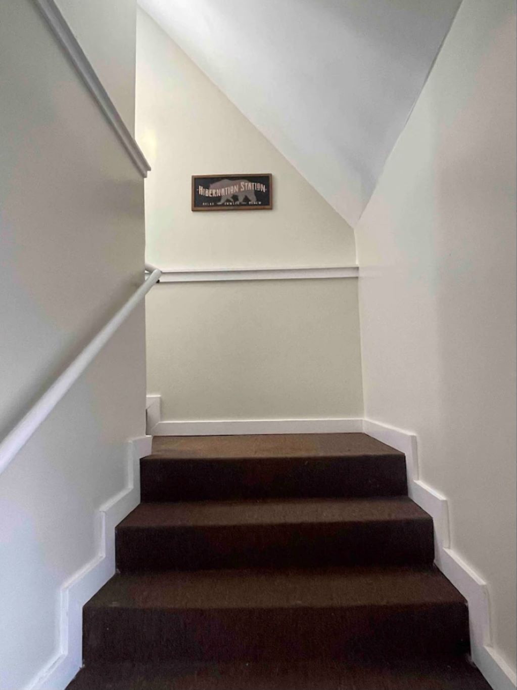 A staircase with dark carpeted steps and white walls.