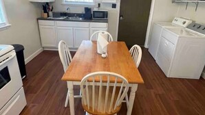 Una cocina compacta con armarios blancos, una mesa de comedor de madera y un horno empotrado.