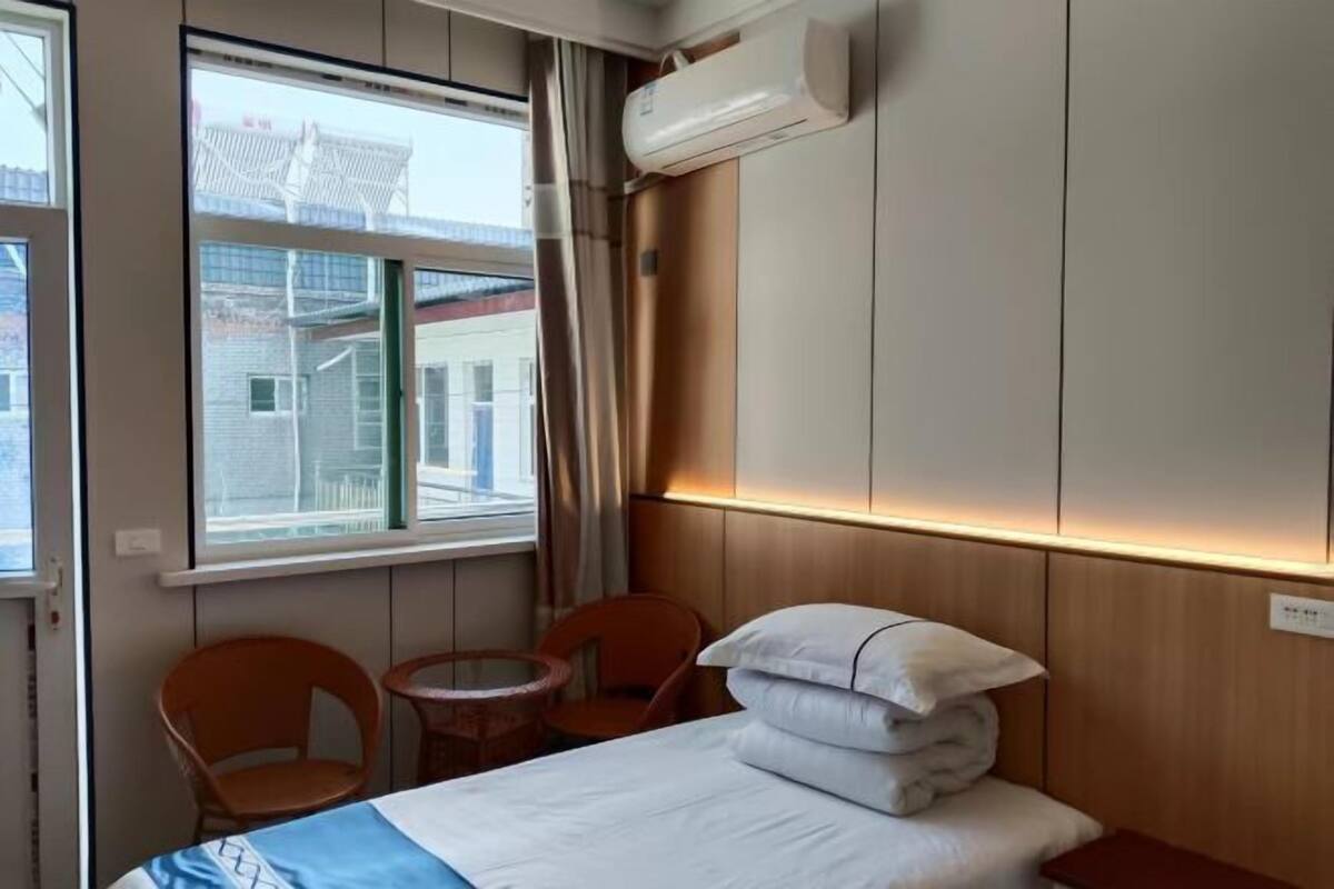 Et hotelværelse med en seng, to stole, et lille bord og et vindue med gardiner.