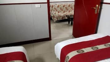 A hotel room with two beds, each with a red and white bedspread, a wooden wardrobe, and a small table with a floral tablecloth.
