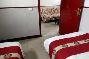 Ein Hotelzimmer mit zwei Betten, jedes mit einer rot-weißen Tagesdecke, einem Holzschrank und einem kleinen Tisch mit einer blumigen Tischdecke.
