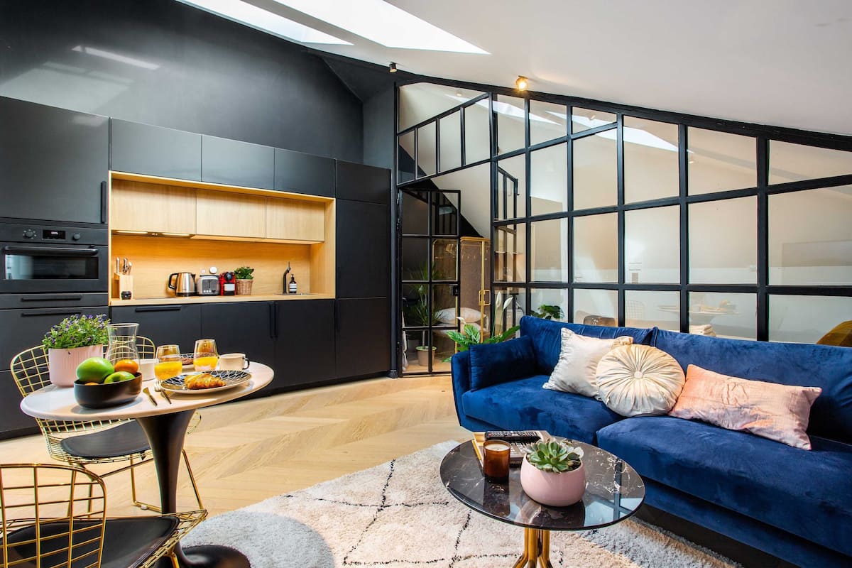 A modern living space with a kitchen, a blue sofa, and a dining area with a table set for breakfast.