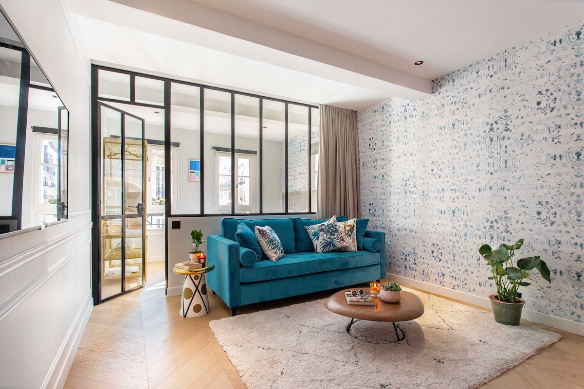A modern living room with a teal sofa, a coffee table, and two potted plants.