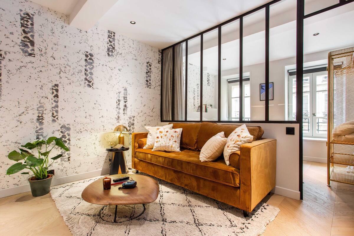 A modern living room with a brown sofa, a coffee table, and a large window.