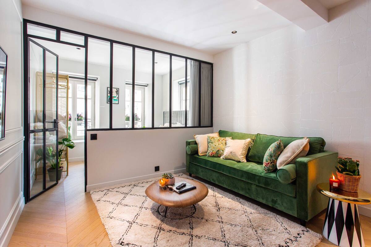 A modern living room with a green sofa, a coffee table, and a large window with black frames.