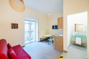 Ein modernes Wohnzimmer mit einem roten Sofa, einem Essbereich mit Tisch und Stühlen, einer Küche mit Glasrückwand und einem großen Fenster, das für natürliches Licht sorgt.