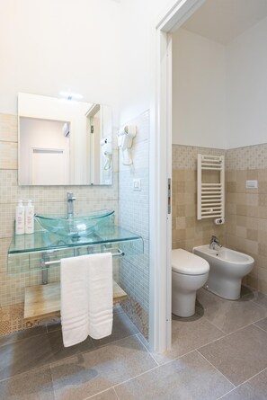 Ein modernes Badezimmer mit Waschbecken aus Glas, zwei Toiletten, einem Bidet und einem Handtuchhalter.