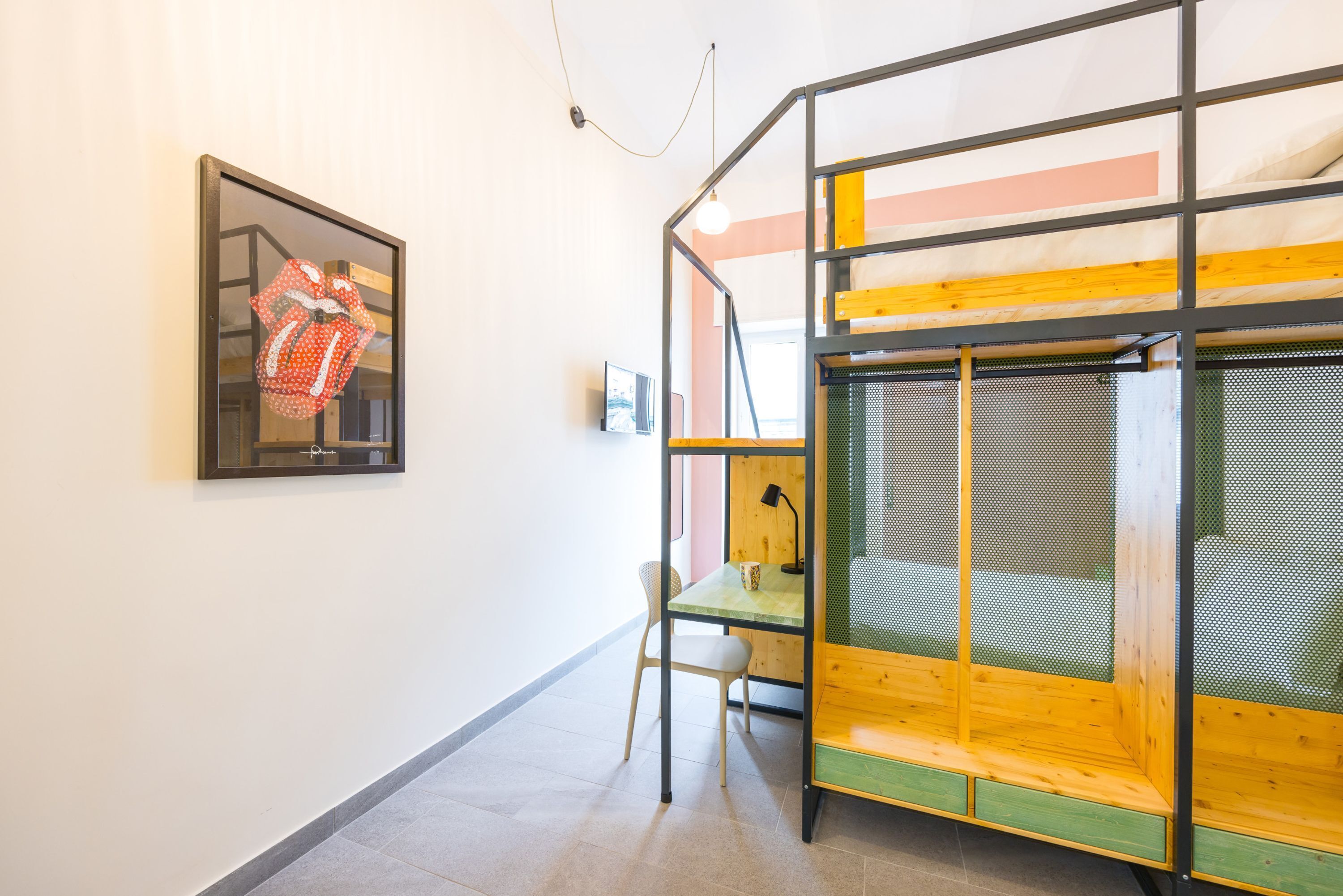 A room with a bunk bed, a framed artwork, a chair, and a small table.
