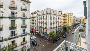 Une vue de rue d’une ville avec des immeubles à plusieurs étages, une rue pavée et des voitures garées.