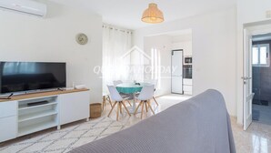 A modern living room with a flat-screen TV, a dining area with a table and chairs, and a kitchen visible through an open door. - Villa La Zenia close to Beach, private pool, walking distance of Zenia Boulevard (Orihuela)