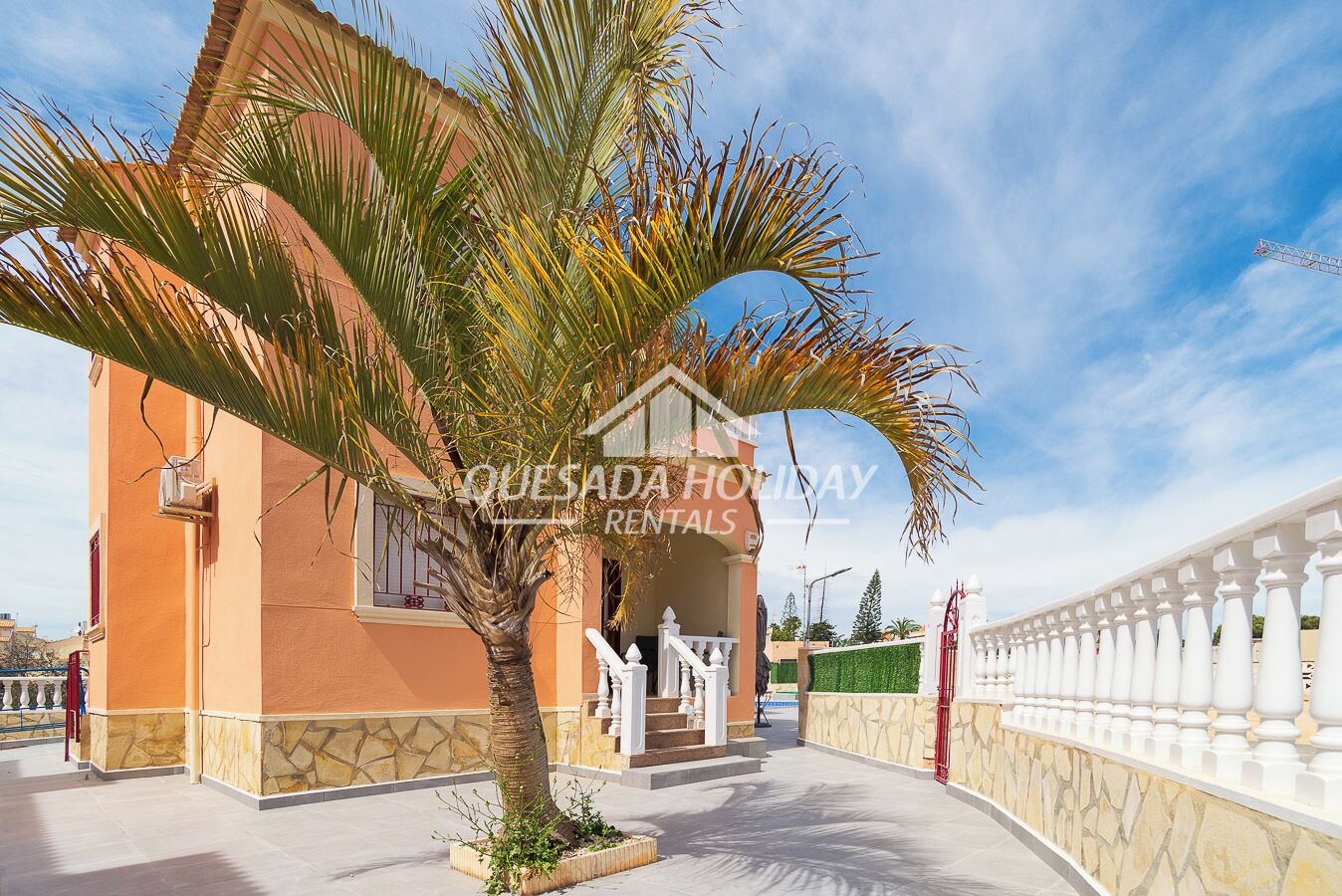 A two-story building with a balcony and a palm tree in front.