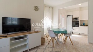 A modern living room with a flat-screen TV, a dining table with chairs, a kitchen area with appliances, and a clock on the wall. - Villa La Zenia close to Beach, private pool, walking distance of Zenia Boulevard (Orihuela)