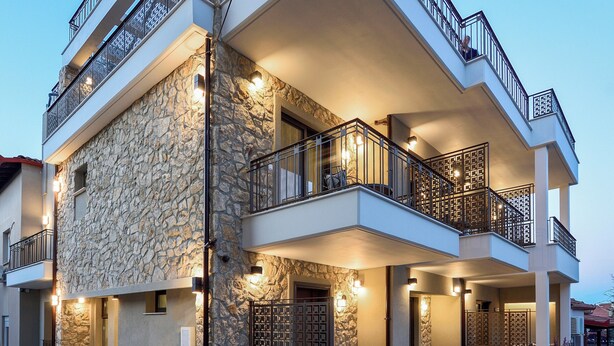 A multi-story building with balconies, stone facade, and outdoor seating area. - Epineio Comfort Living (Dio-Olympos)