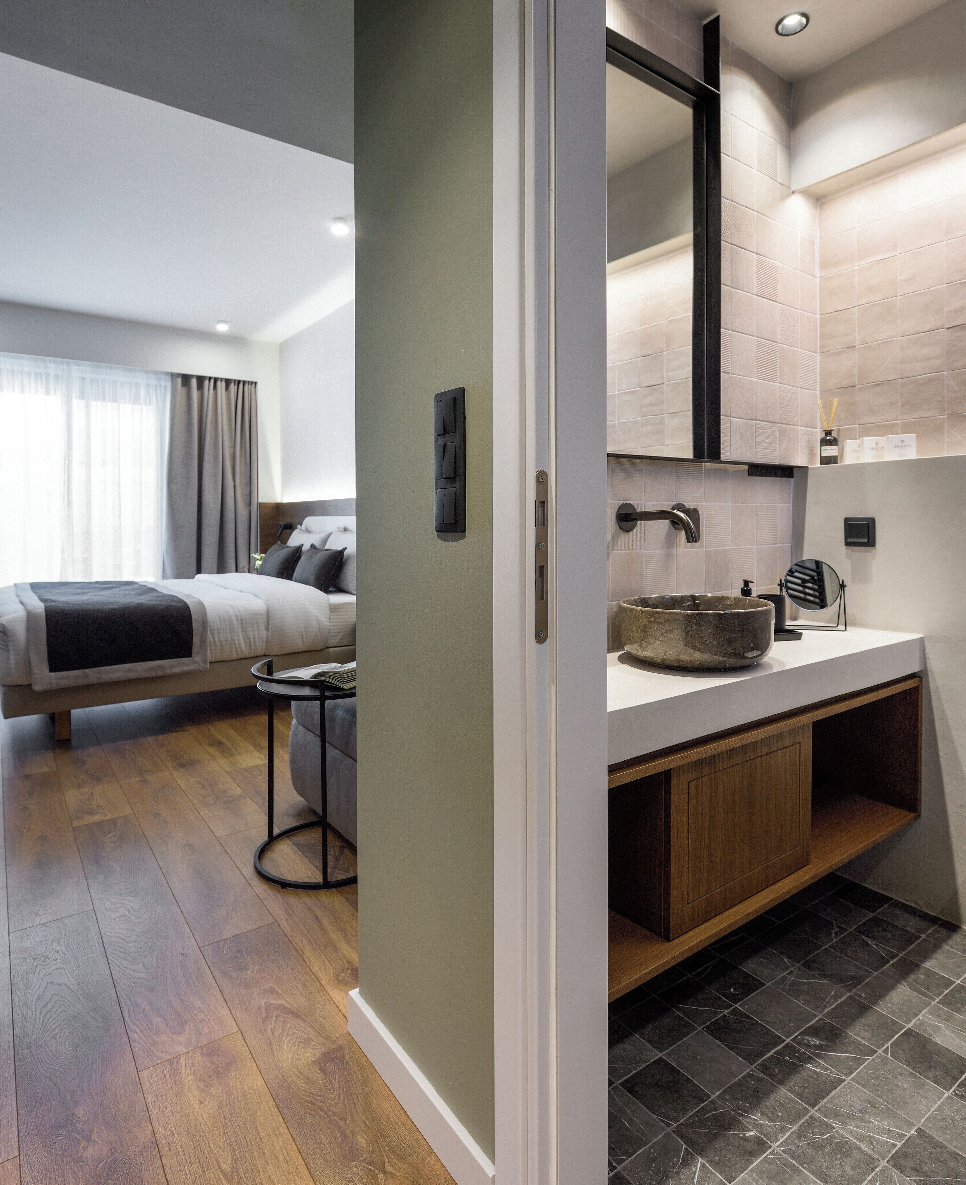 A modern hotel room with a bed, bedside table, and a bathroom with a sink and mirror.