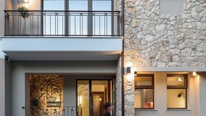 A hotel entrance with a stone facade, a balcony with metal railings, and a person walking by. - Epineio Comfort Living (Dio-Olympos)