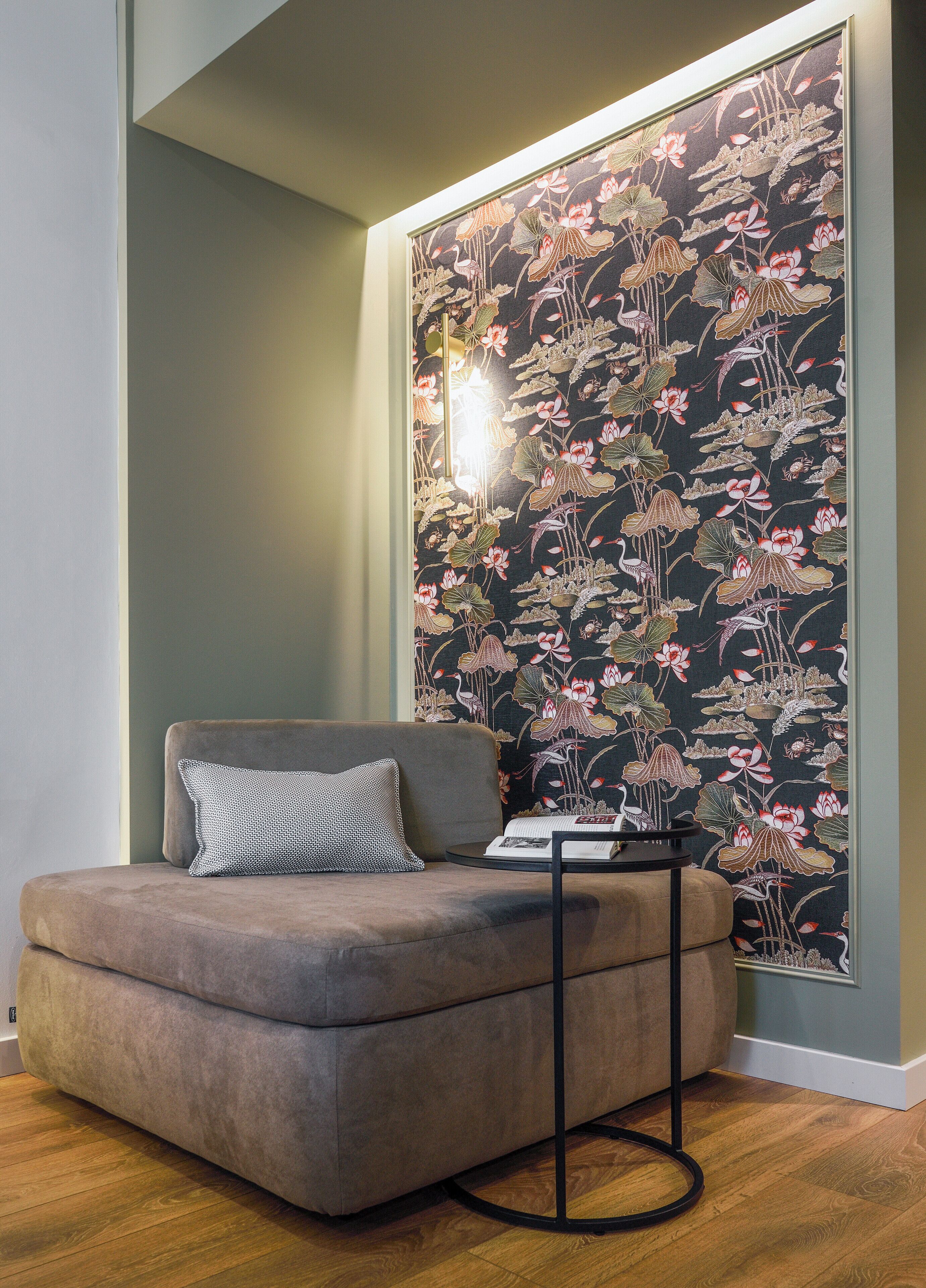 A modern living room with a sofa, a side table, and a decorative wall with a floral pattern.
