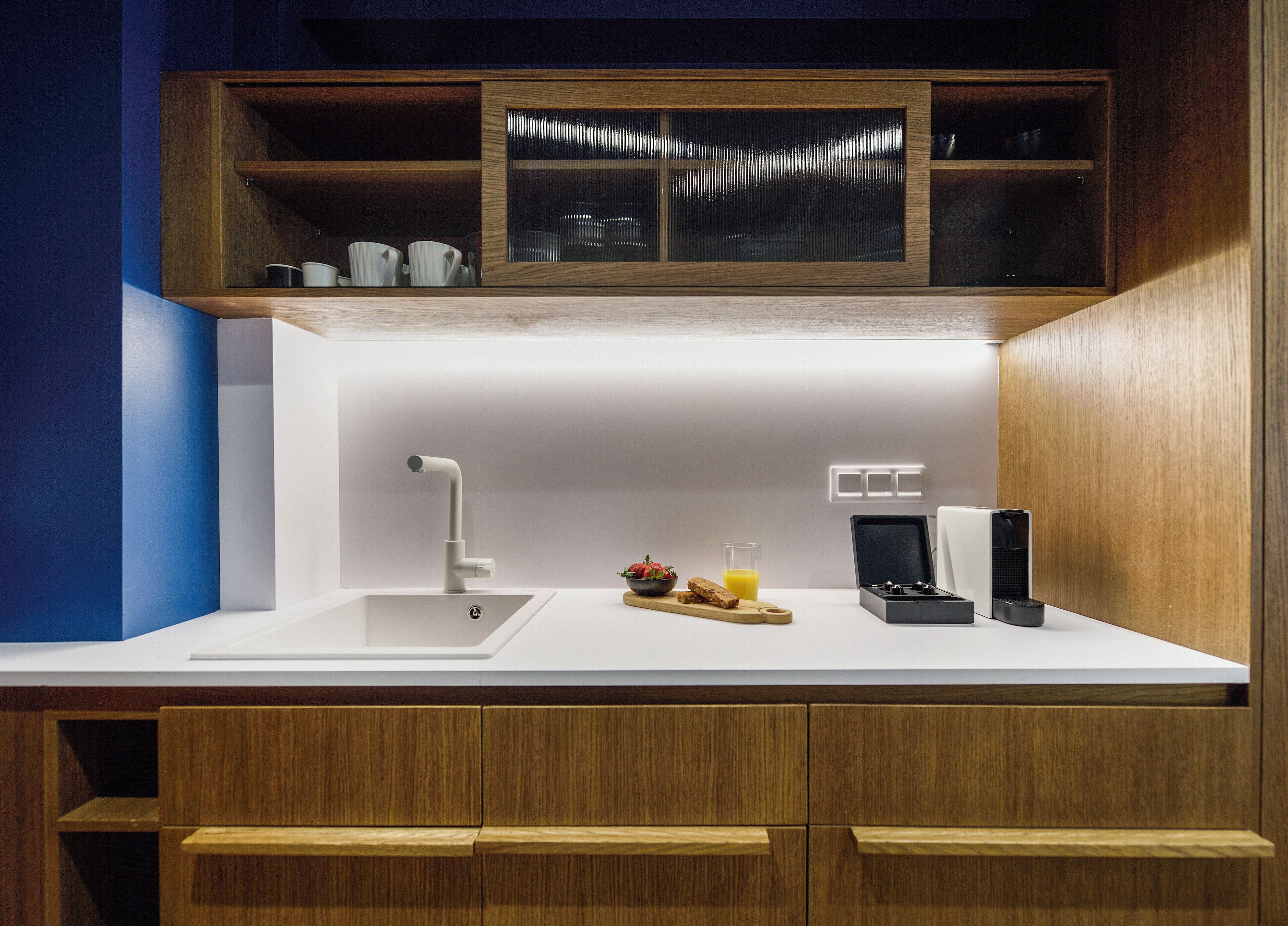 Une cuisine moderne avec un plan de travail blanc, des armoires en bois, un évier en acier inoxydable et un four à micro-ondes encastré.