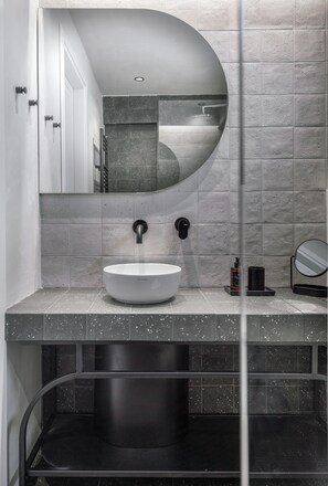 A modern bathroom with a white sink, a large mirror, and a shower. - Epineio Comfort Living (Dio-Olympos)