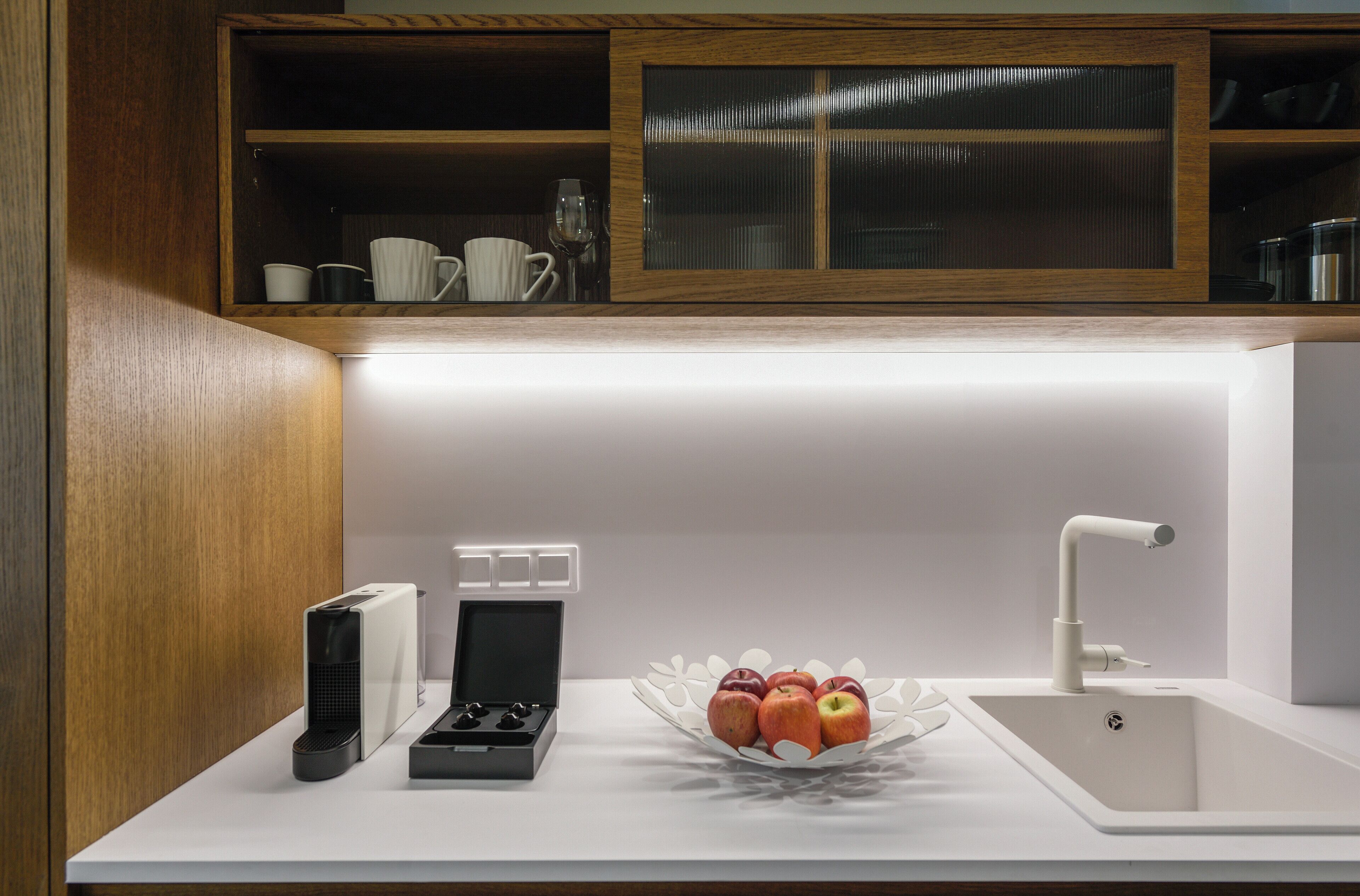 Une cuisine moderne avec un plan de travail blanc, un évier et un saladier rempli de pommes.