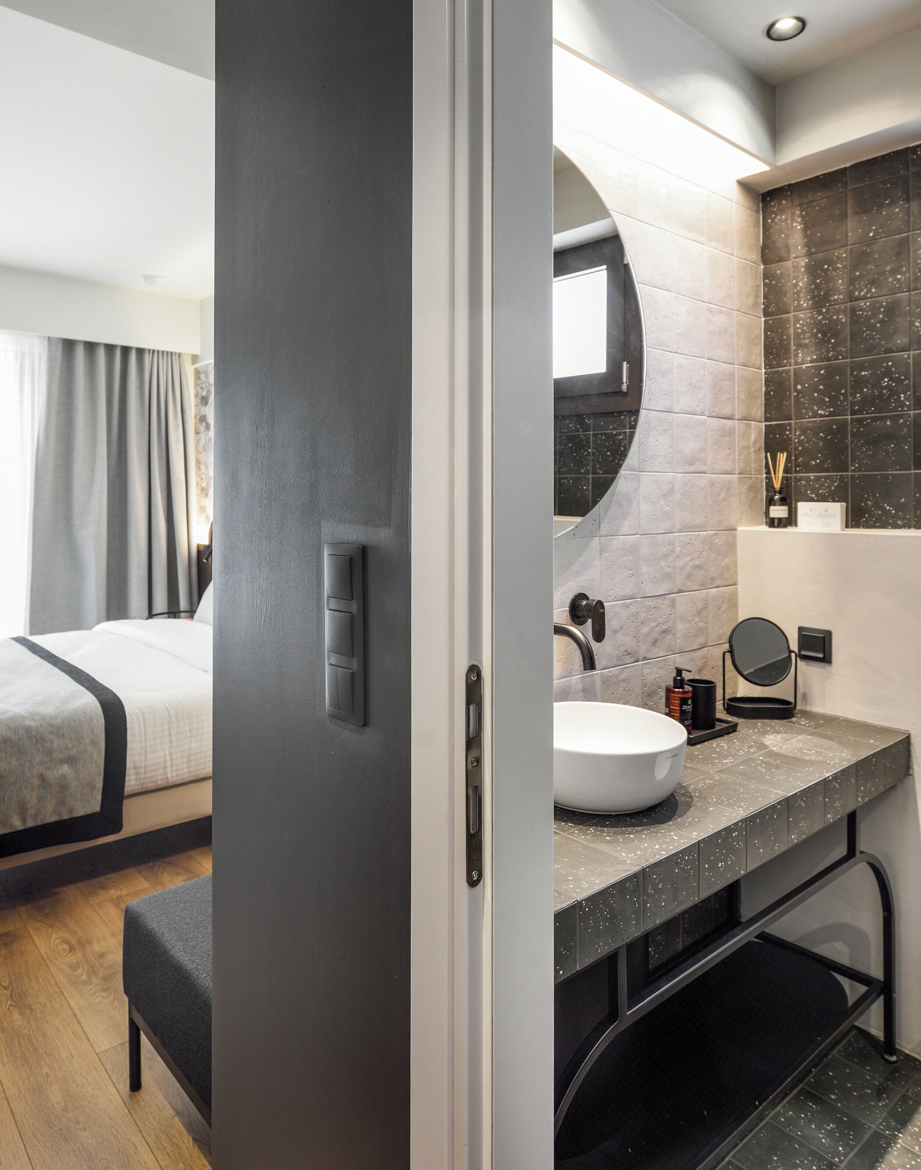 A modern hotel room with a bed, a bathroom with a round mirror, and a sink.