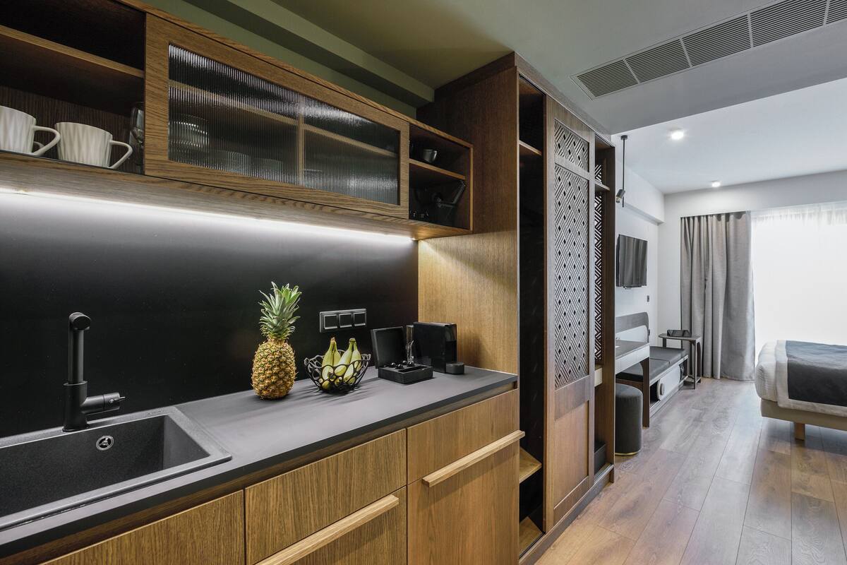 A modern kitchen with wooden cabinets, a black countertop, and a sink. There is a fruit bowl with bananas and a pineapple on the counter.
