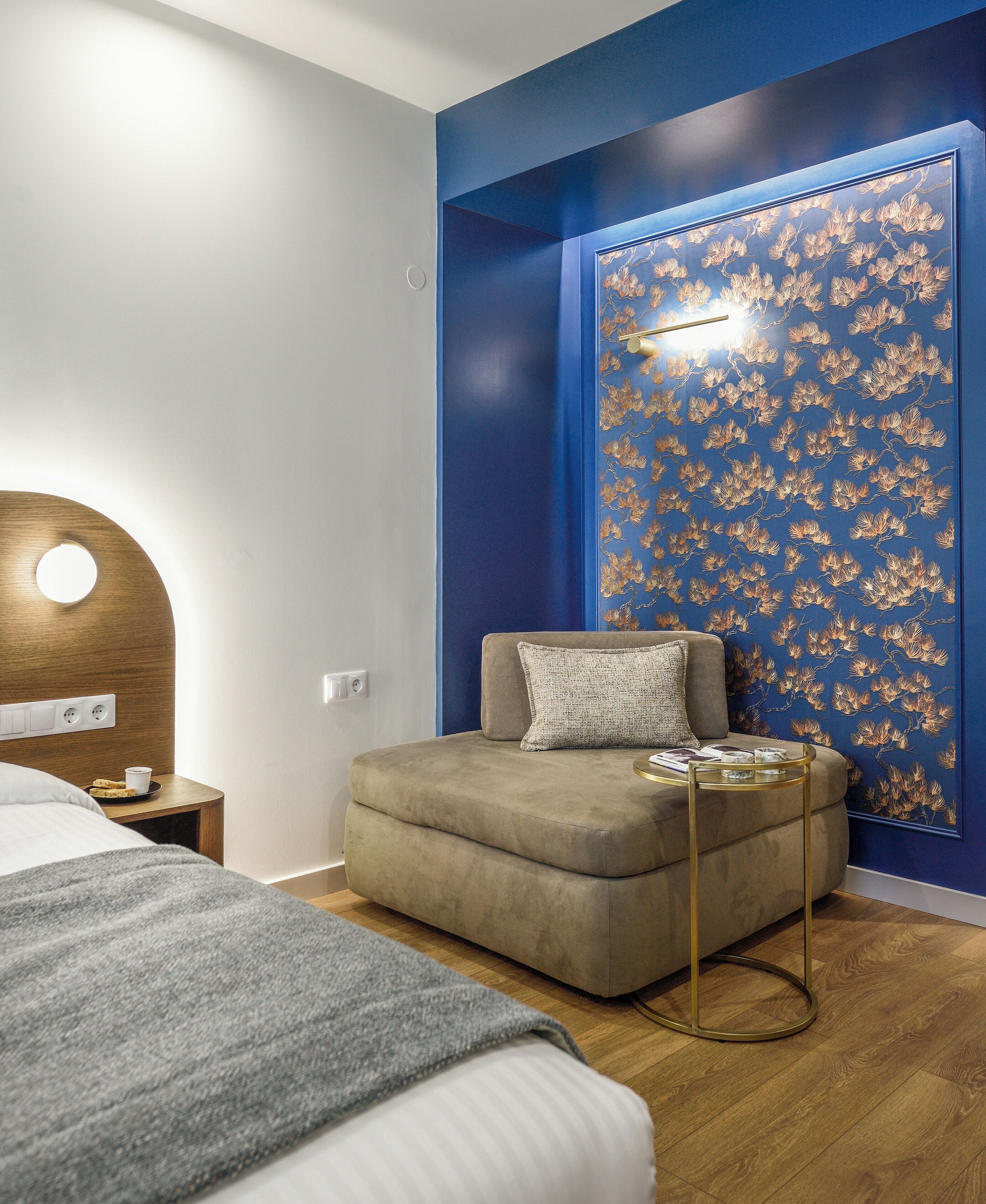 A modern bedroom with a bed, a small sofa, and a wall with a blue floral wallpaper.