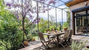 A wooden deck with a table and chairs, surrounded by potted plants and trees. - Pomerolle - Saoû - 4 pers (Saou)