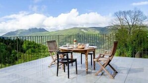 En terrasse med et rundt bord og fire stole, med udsigt over et bjergrigt landskab.