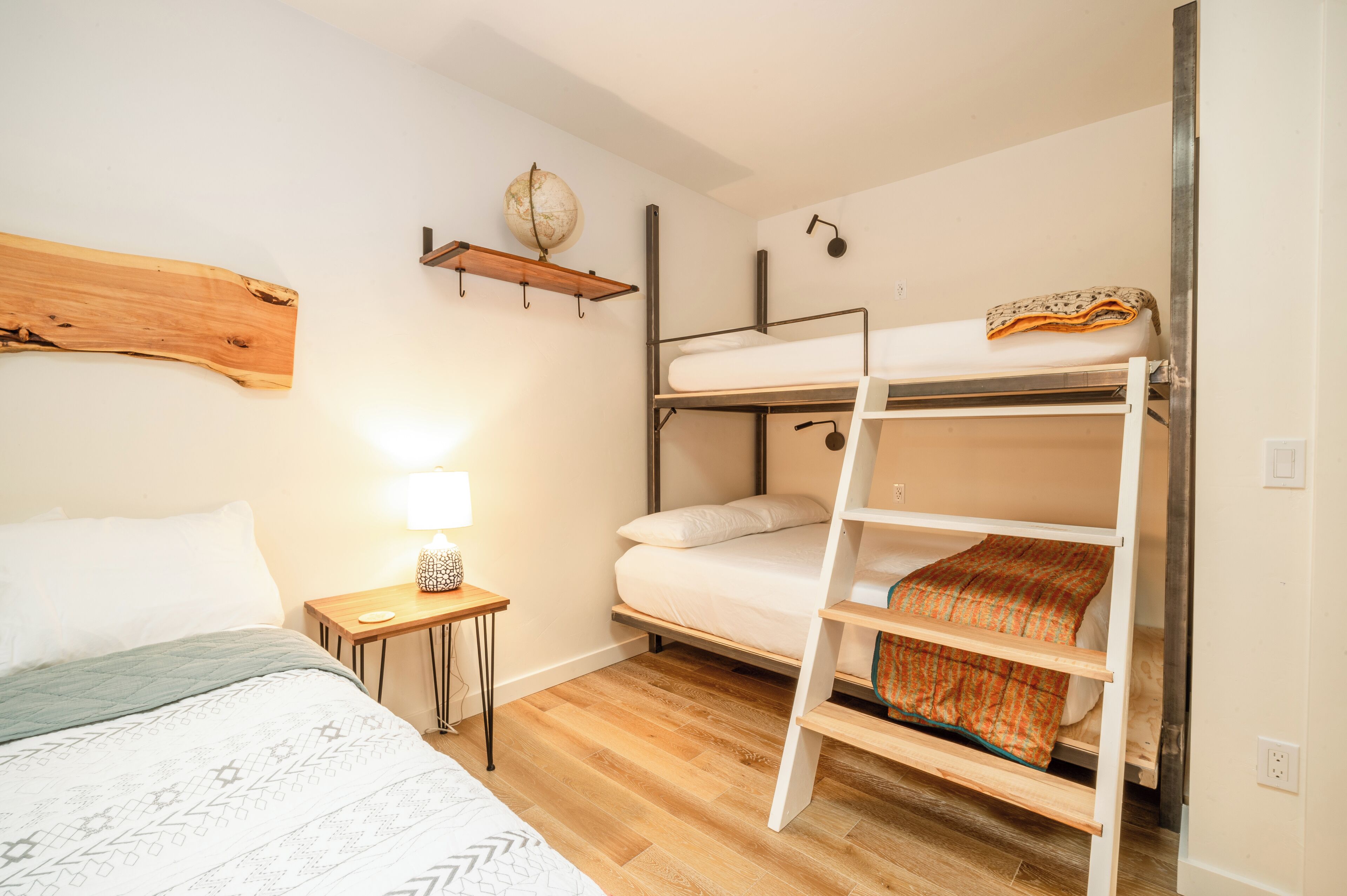 Una cama litera con una escalera, una mesita de noche con una lámpara y un estante de madera con un globo terráqueo.