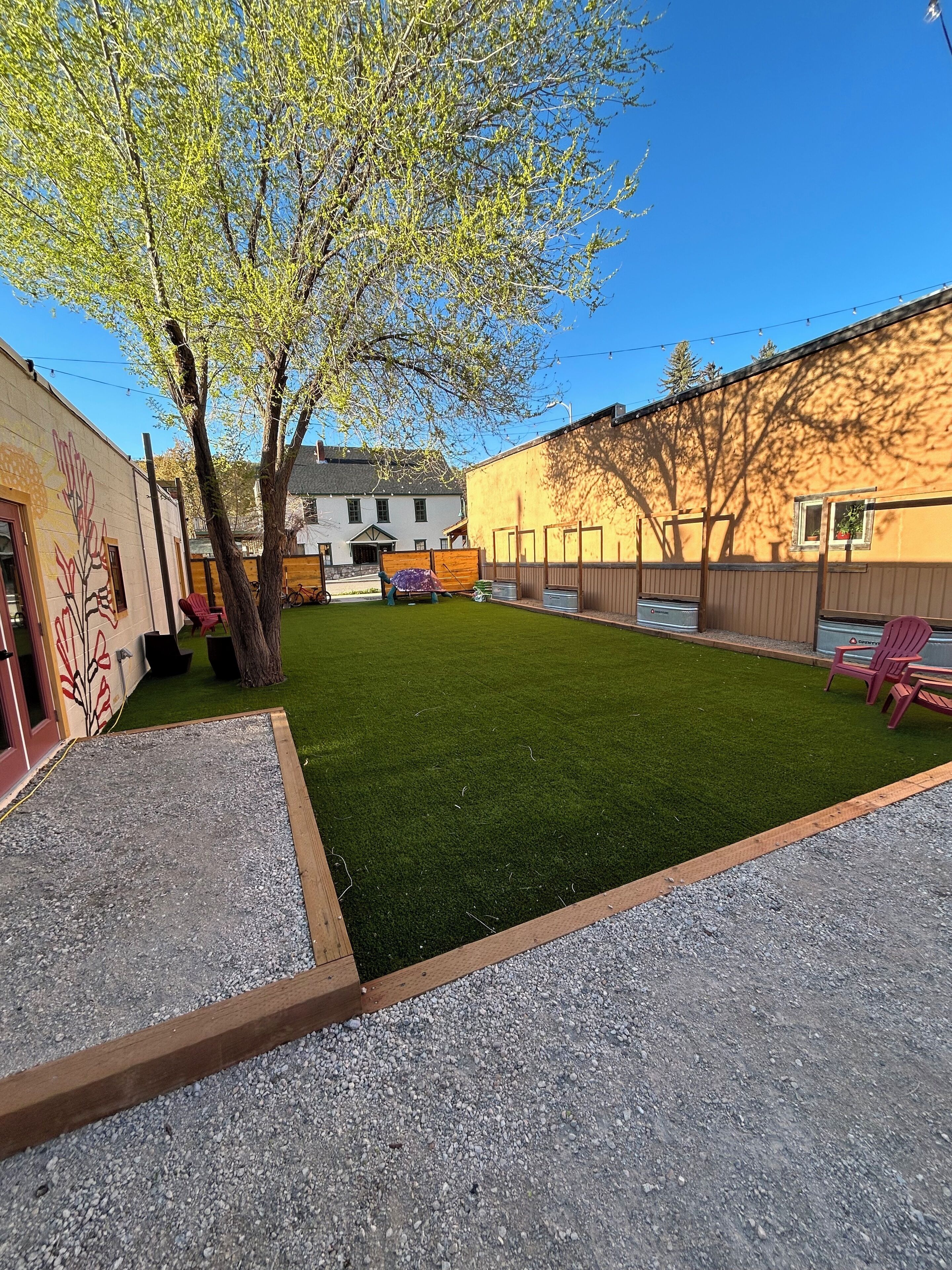 A backyard with artificial grass, a wooden fence, and a building with a mural.