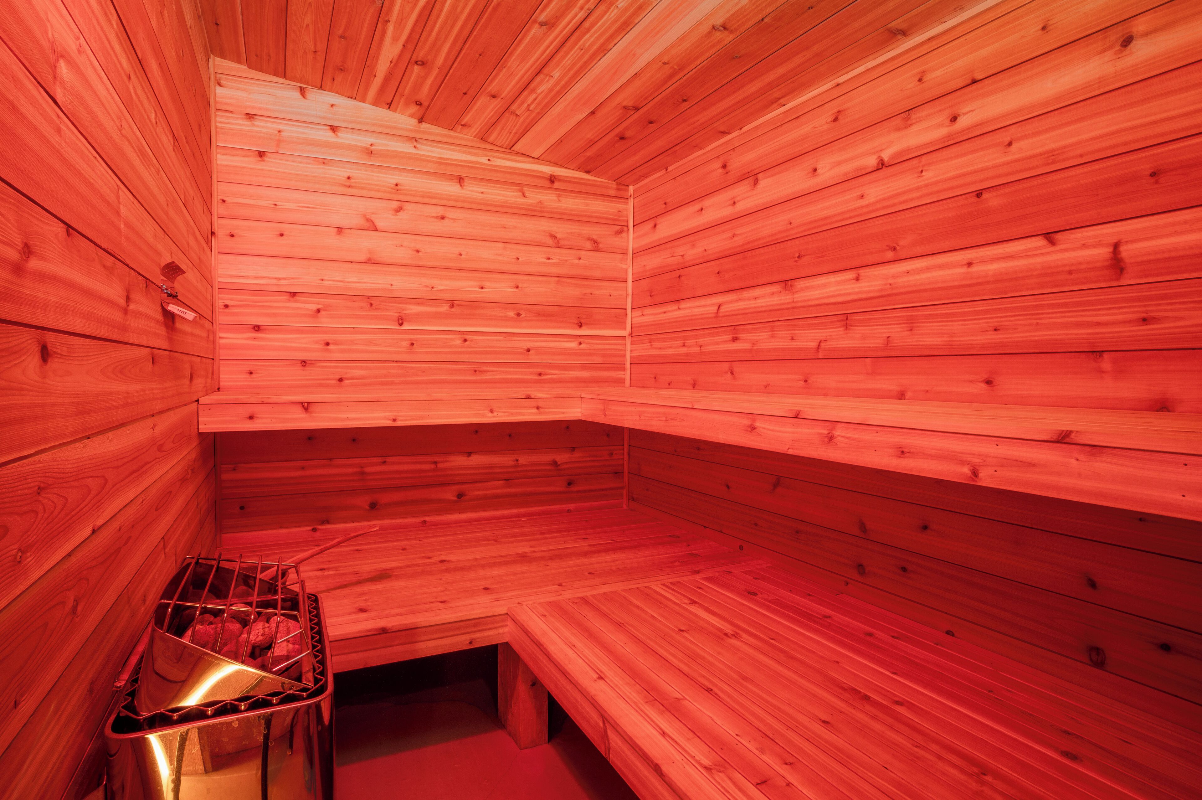 Una sauna con paredes y bancos de madera, un banco de metal y un calentador visible.