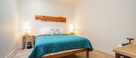 A bedroom with a bed, bedside lamps, a wooden headboard, a small table, and a rug.
