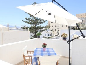 Een balkon met een tafel, stoelen, een witte parasol en potplanten.