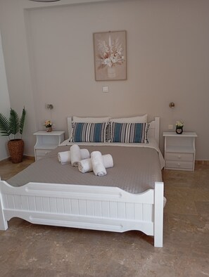 A bedroom with a white bed, two nightstands, a wall-mounted light, and a framed floral artwork. - Sea View And Mountain View Apartment For 4 People (Ierapetra)