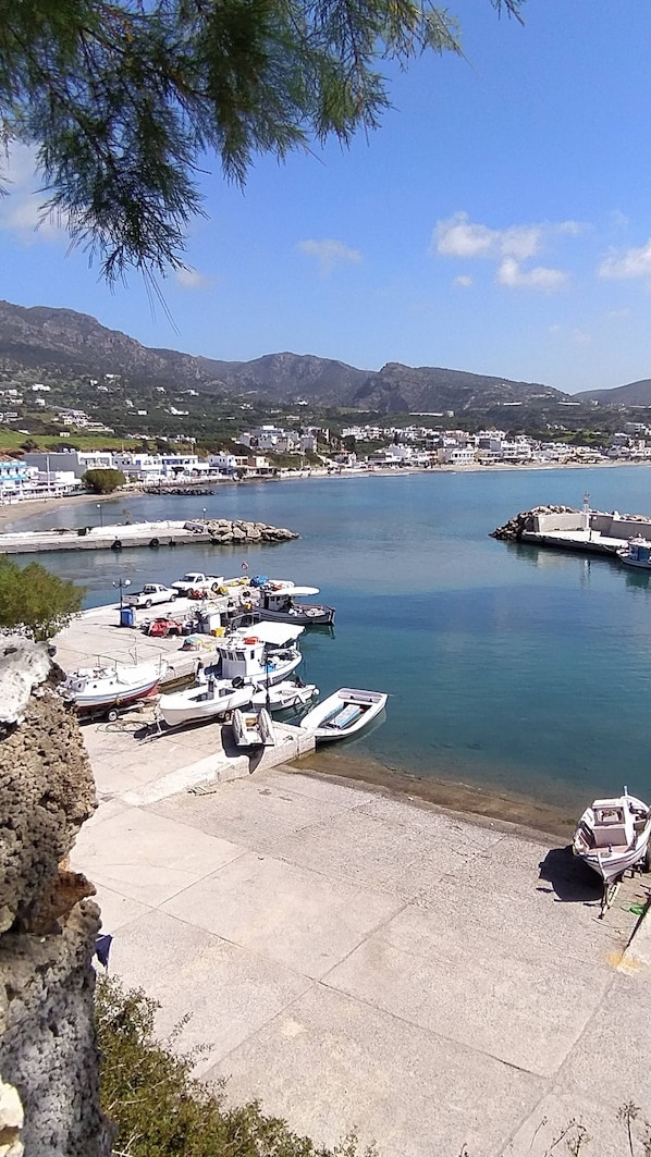 A coastal marina with boats docked, a clear sky, and a mountainous backdrop.
