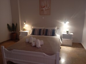 A bedroom with a bed, two bedside tables, a nightstand, a potted plant, and a wall-mounted light fixture. - Sea View And Mountain View Apartment For 4 People (Ierapetra)