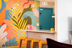 Cozinha com um mural colorido, uma porta verde-água e banquetas amarelas.