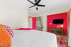 A bedroom with a bed, a ceiling fan, a television, and a red wall.